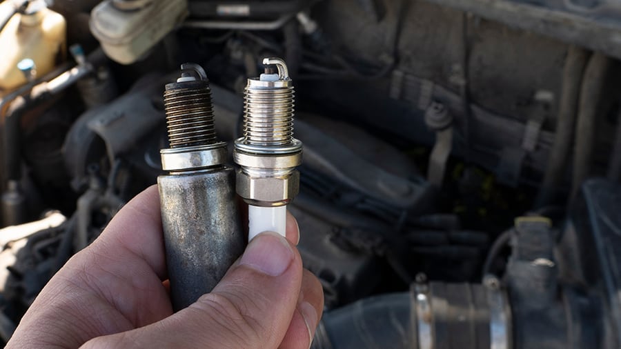 A new spark plug held next to an old one.