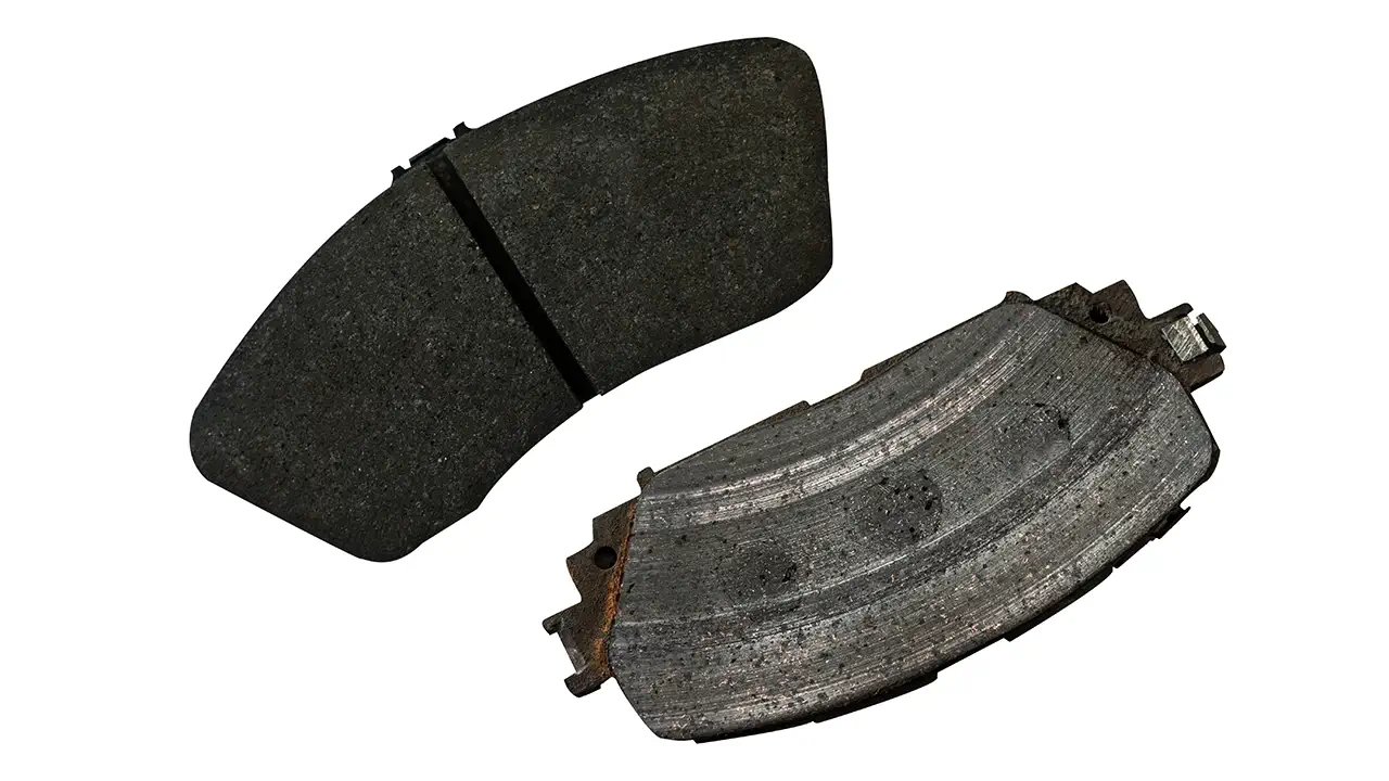 A badly worn brake pad is set beside a new pad for comparison.